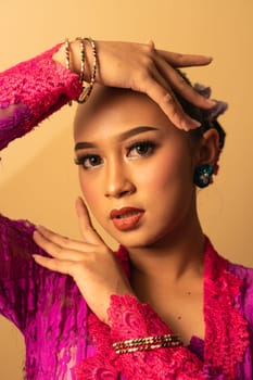 beautiful Balinese woman wearing makeup in a pink dress while posing with exotic hands inside the studio