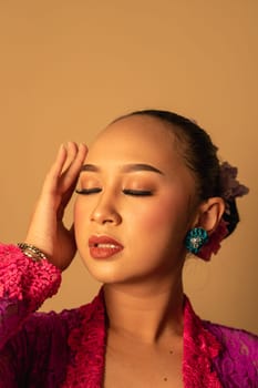 Portrait of Balinese woman with pink dress pose with hands on the face inside the room