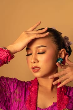 Portrait of Balinese woman with pink dress pose with hands on the face inside the room