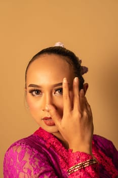Portrait of Balinese woman with pink dress pose with hands on the face inside the room