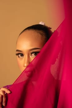 A beautiful Balinese woman covered her makeup face with red fabric from the dress inside the studio