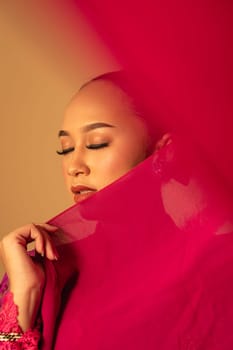 A beautiful Balinese woman covered her makeup face with red fabric from the dress inside the studio