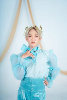 an elegant woman with blonde hair wearing a golden crown and a blue dress in a white room