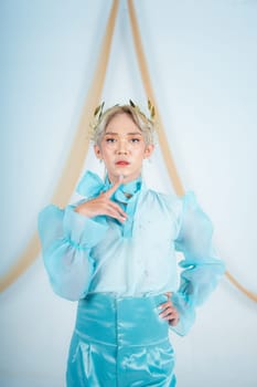 an elegant woman with blonde hair wearing a golden crown and a blue dress in a white room