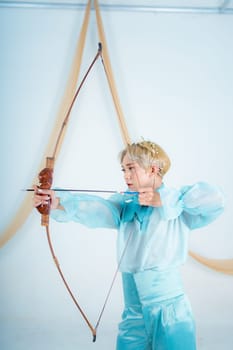 an Asian woman with blonde hair holding an arrow while wearing a blue dress in a white room