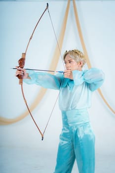 an Asian woman with blonde hair holding an arrow while wearing a blue dress in a white room