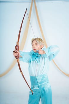an Asian woman with blonde hair holding an arrow while wearing a blue dress in a white room