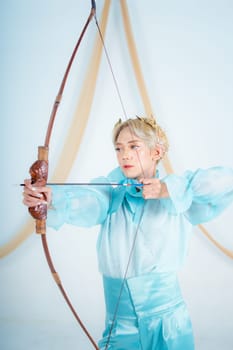 an Asian woman with blonde hair holding an arrow while wearing a blue dress in a white room