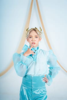 an elegant woman with blonde hair wearing a golden crown and a blue dress in a white room