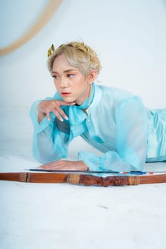 a princess in a blue dress posing on the floor with a bow in a white room