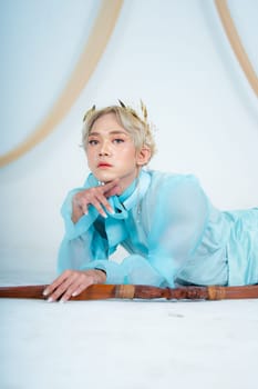 a princess in a blue dress posing on the floor with a bow in a white room