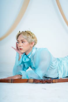 a woman with blonde hair and a face full of makeup poses beautifully with a bow in a white studio