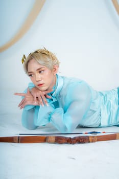 a princess in a blue dress posing on the floor with a bow in a white room