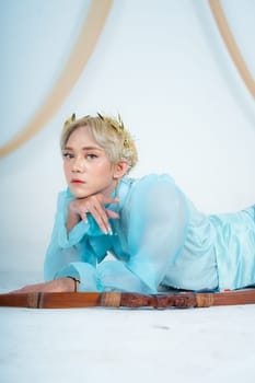 a woman with blonde hair and a face full of makeup poses beautifully with a bow in a white studio