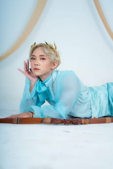 a woman with blonde hair and a face full of makeup poses beautifully with a bow in a white studio