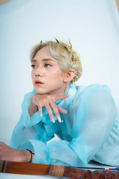 a woman with blonde hair and a face full of makeup poses beautifully with a bow in a white studio