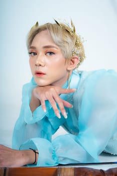 a woman with blonde hair and a face full of makeup poses beautifully with a bow in a white studio