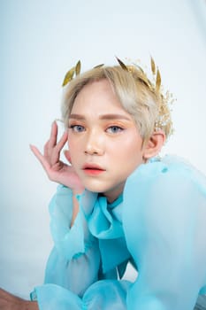 a woman with blonde hair and a blue dress posing with curled arms and a blushing face in front of a white background