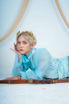 a woman with blonde hair and a face full of makeup poses beautifully with a bow in a white studio