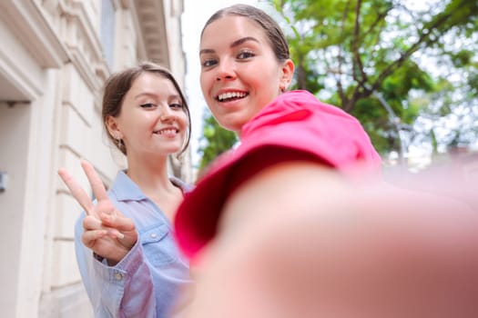 Caucasian women smiling closely while taking a selfie together on a city street. Outdoor setting with trees and buildings, capturing a joyful and candid moment of friendship and connection