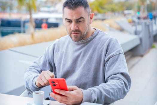 serious caucasian man, serious man looking at her mobile smart phone, typing a message on the terrace of an outdoor cafe. Addiction to social networks. App, device technology concept.