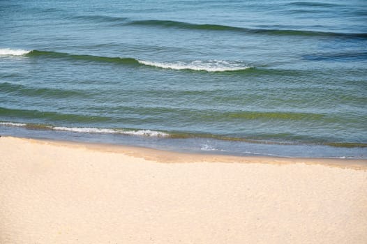 Clean sandy beach, blue sea. Calm waves roll onto the sand. Soft wave of the sea. High quality photo