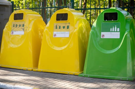Garbage collection containers for recycling against city background. Yellow, blue containers for recycling plastic, paper and glass waste. Environmental awareness, recycling, waste management concept. High quality photo