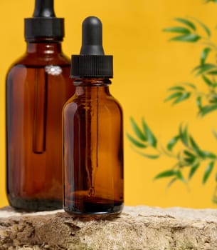 Amber glass dropper bottles on a natural stone surface with a yellow background and green plant elements. Ideal for cosmetics, essential oils, or herbal extracts.