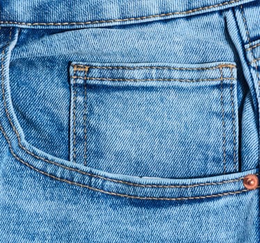 Close up of blue denim jeans showing a front pocket corner with distinct orange stitching detail