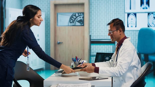 Male doctor evaluating x ray imaging and lab test results, consulting hospital records to provide the report for a sick patient. Healthcare specialist ensuring recovery plan on insurance. Camera A.
