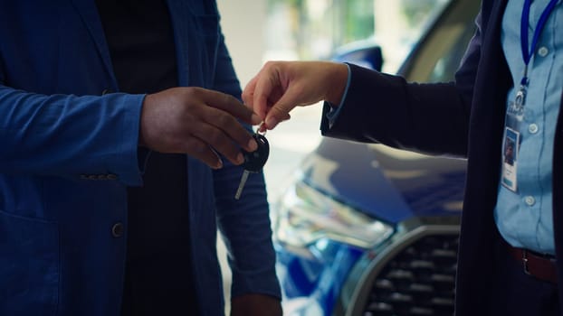 Showroom dealer signing forms for customers after finishing deal, shaking hands. Dealership agent completes documentation for vehicle sale, giving car keys, camera A close up