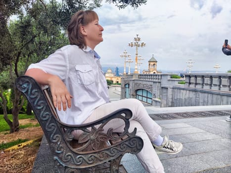 Blonde adult woman sits contemplatively on a bench, taking in the beautiful surroundings of a popular excursion spot during her travels.