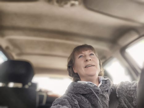 A mature blonde woman enjoys a joyful moment capturing a selfie in her car, smiling brightly while navigating the road on a sunny day.