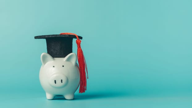 Piggy bank wearing graduation cap on blue background. Symbol of saving money, student loans, tuition fees, and financial planning for education.