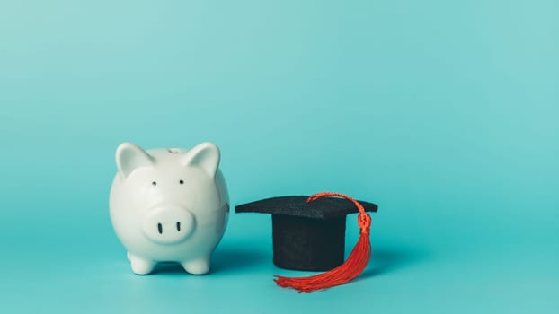 Piggy bank with graduation cap on blue background. Symbol of saving money, student loans, tuition fees, and financial planning for education.
