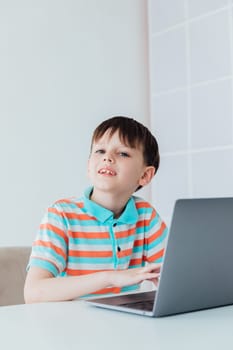 Boy schoolboy learning games at the table with laptop online