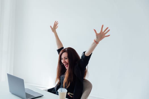 brunette woman working on a table with a laptop shouting happily laughing