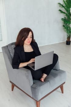 Brunette woman working on chair with laptop online from home