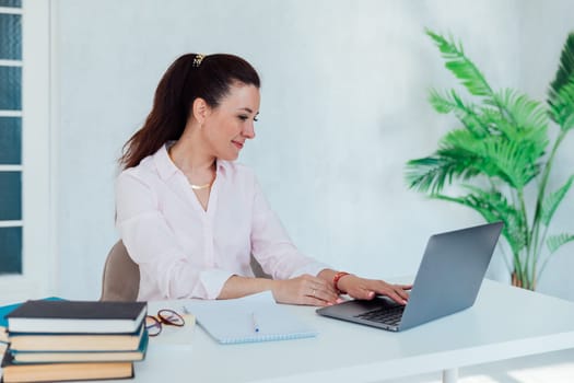 brunette woman working in office at desk with laptop and documents