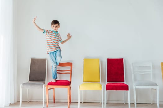 Little boy happily jumping on different chairs in white room