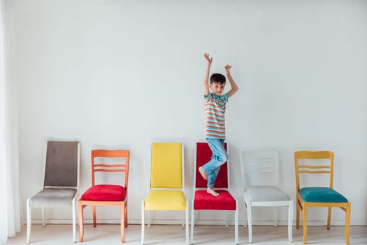 Little boy happily jumping on different chairs in white room