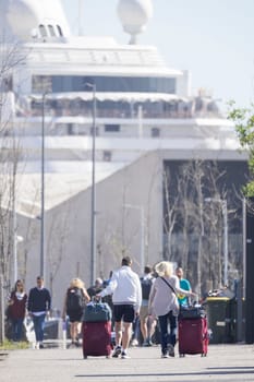 Tourists pulling rolling suitcases walking towards large cruise ship in barcelona, spain
