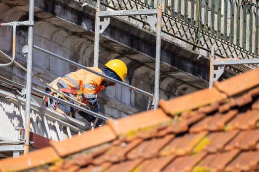 Construction worker wearing safety equipment and repairing the facade of an old building using scaffolding