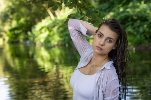 Moody portrait of beautiful brunette girl with wet hair posing in the river. Horizontally. 