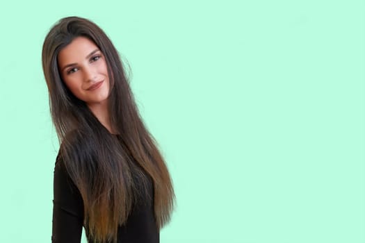 Studio waist up portrait of a tanned beautiful brunette long haired young  woman posing in front of a light green background.