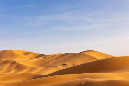 Landscape background. Lowering horizon of sand dunes with prevailing blue sky with clouds. Western Sahara. Morocco. Horizontal.