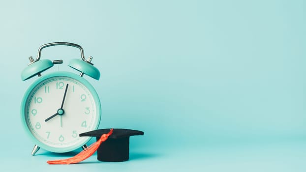 Graduation cap and alarm clock on blue background. Symbol of education, time management, exam preparation, academic success, and back to school concept.