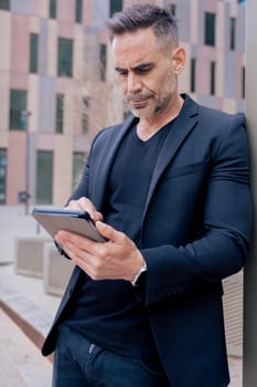 Confident businessman standing outdoors using a tablet in a modern urban setting.He appears focused and professional. Concept of digital work, technology, and contemporary business lifestyle. Vertical