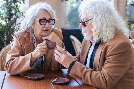 Caucasian senior couple enjoying coffee at an outdoor cafe. The woman speaks closely to the man, creating an intimate and thoughtful moment. Concept of connection, trust, and shared experiences.