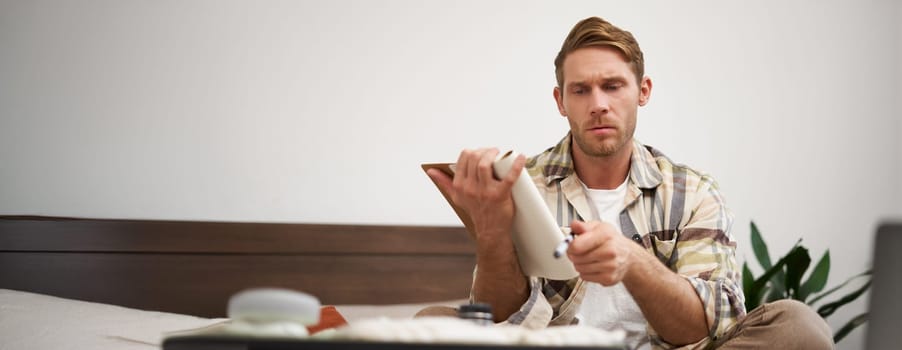 Portrait of thoughtful young man, tourist going on vacation, going through holiday check-list, writing down what he wants to take on travelling.